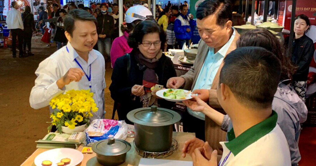 Bà Vũ Kim Hạnh - Chủ tịch Hội doanh nghiệp HVNCLC (đứng thứ hai từ trái qua) thử món ăn nấu bằng nồi sứ dưỡng sinh cao cấp Minh Long.